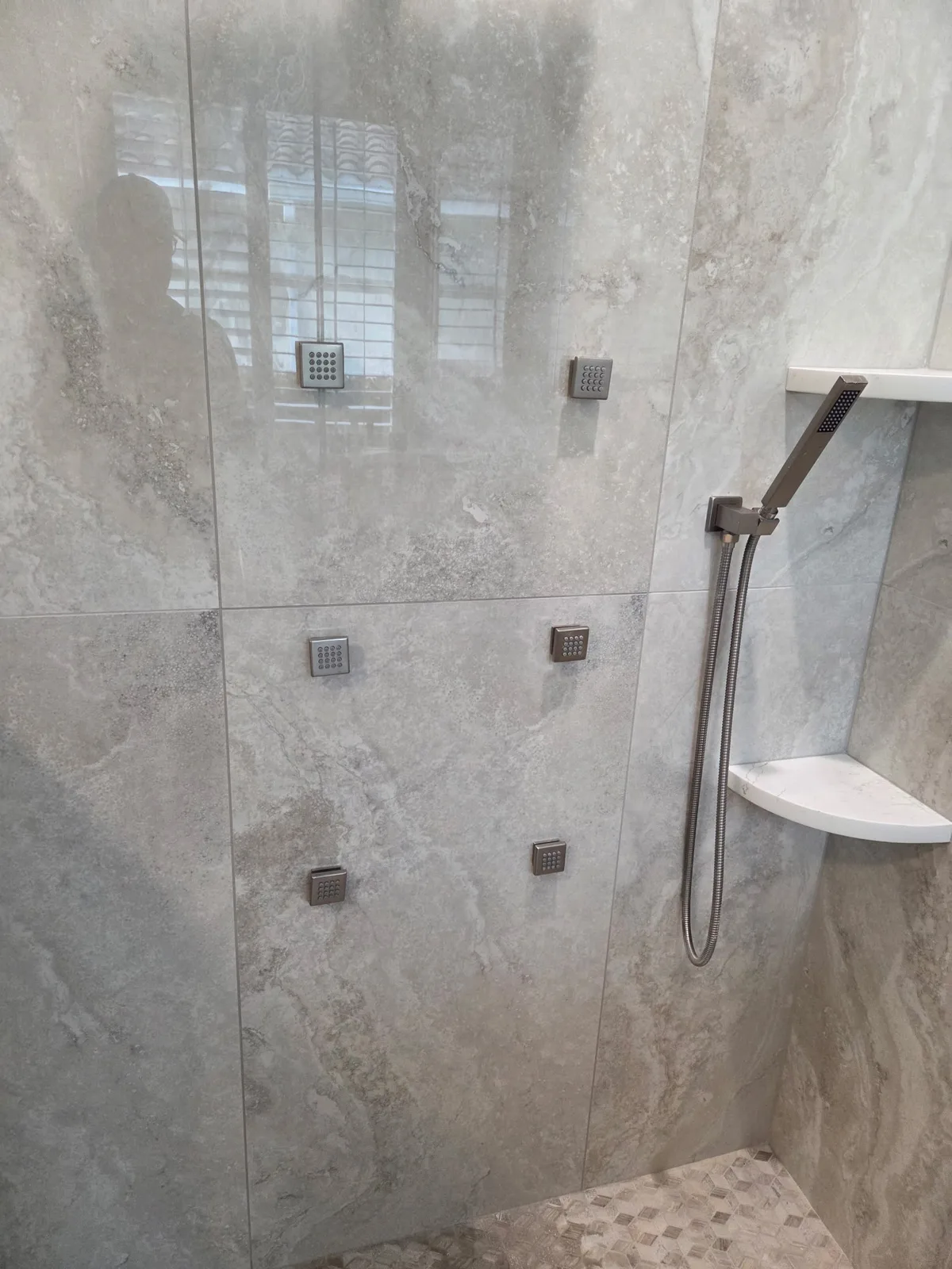 Finished walk-in shower with large gray tile, glass panel, hand shower and corner shelf