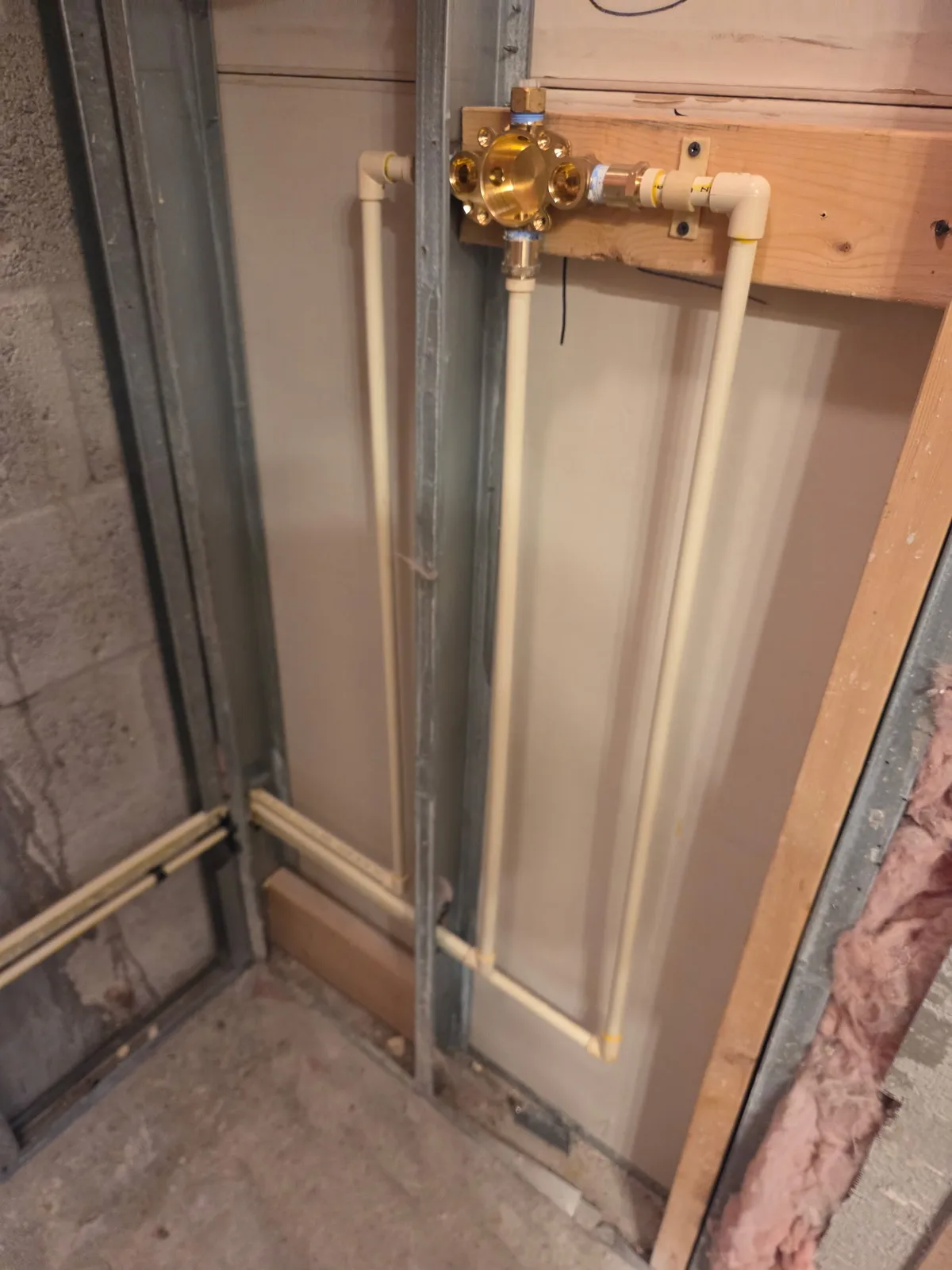 Brass gas shutoff valve mounted on a black iron gas pipe in a framed wall