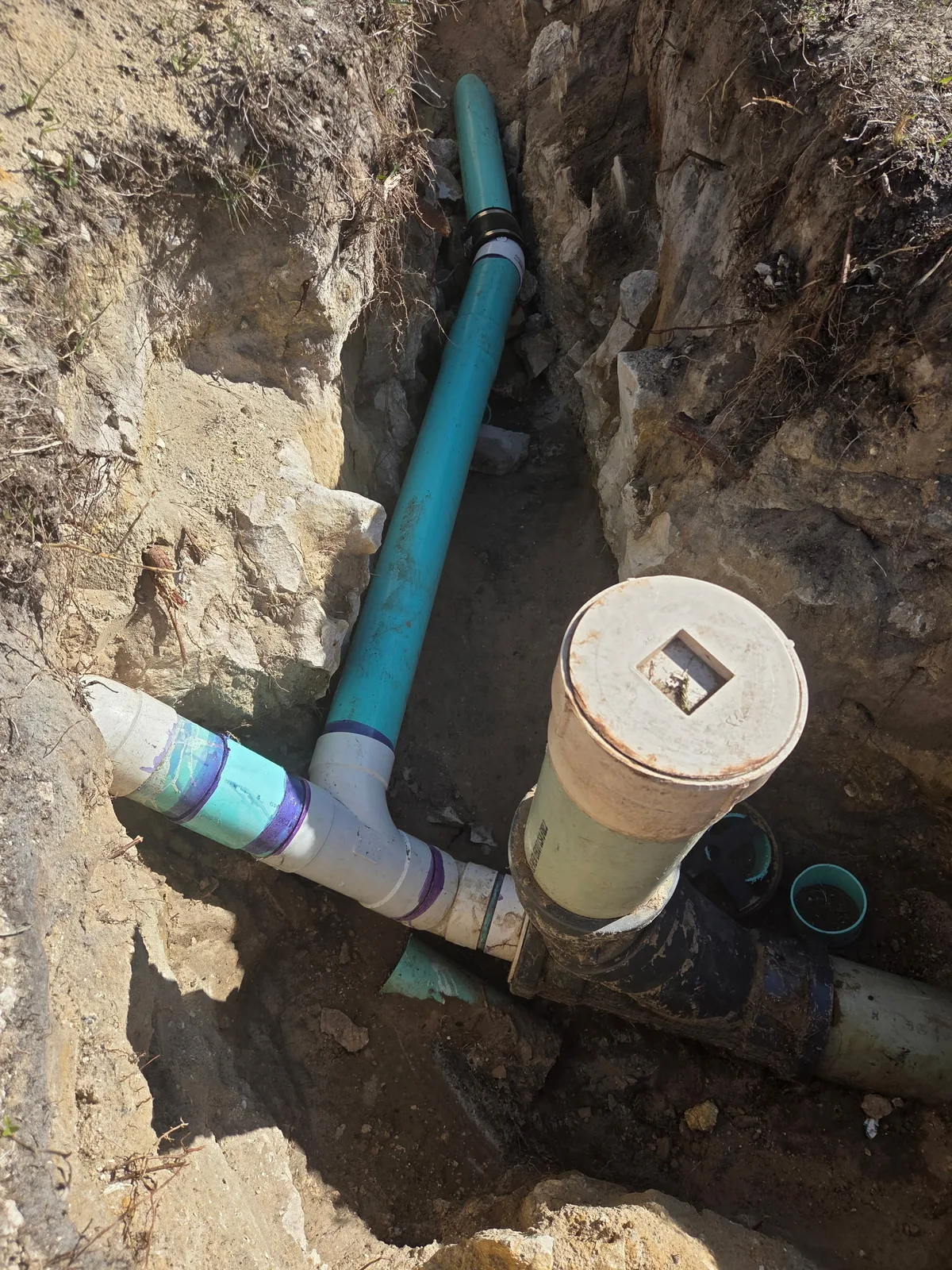 Exposed PVC and cast-iron drain pipe in an open excavation next to a foundation