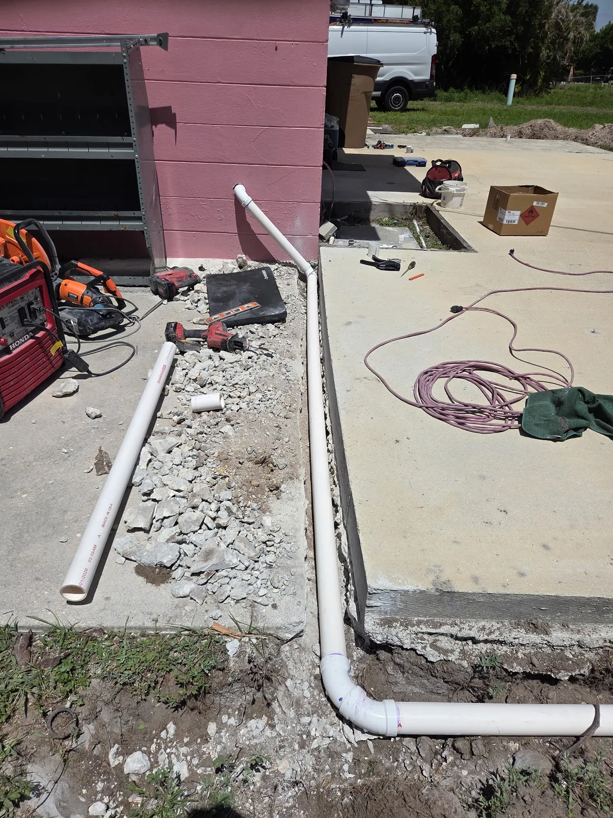 PVC drain and vent stubs exiting a concrete slab beside a house exterior